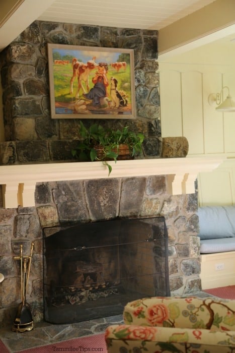 Painting above a rock fireplace with a floral chair in front of it. 