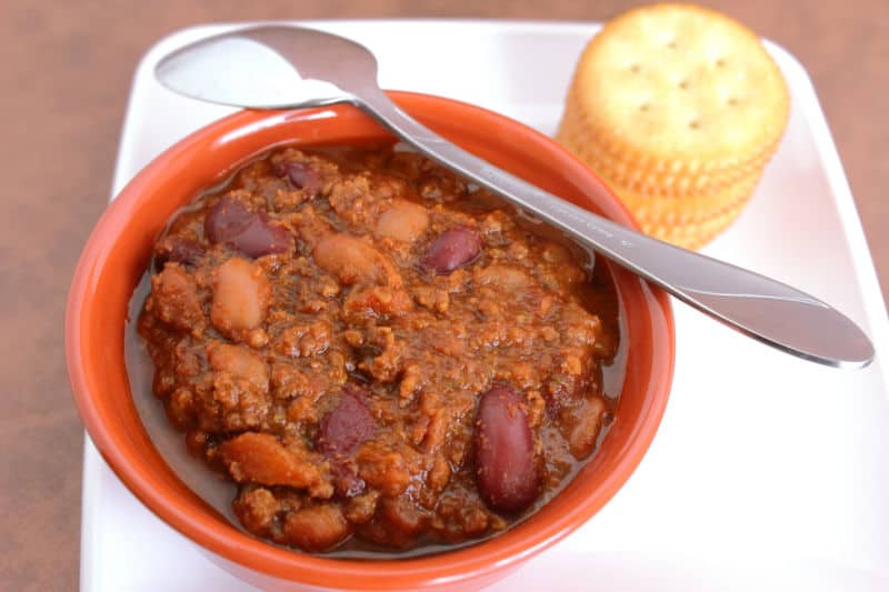 Bowl of Wendy's Chili with a silver spoon and crackers on a white plate
