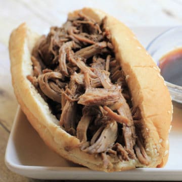 French dip sandwich on a roll next to a bowl of au jus sauce