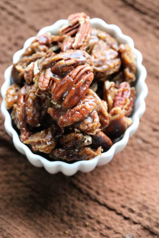Glazed pecans in a white bowl on a brown napkin