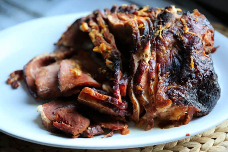 Ham with orange zest on it sitting on a white platter