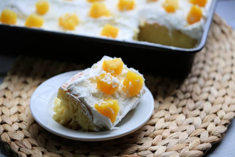 Slice of Pina Colada Poke Cake on a white plate next to the cake pan