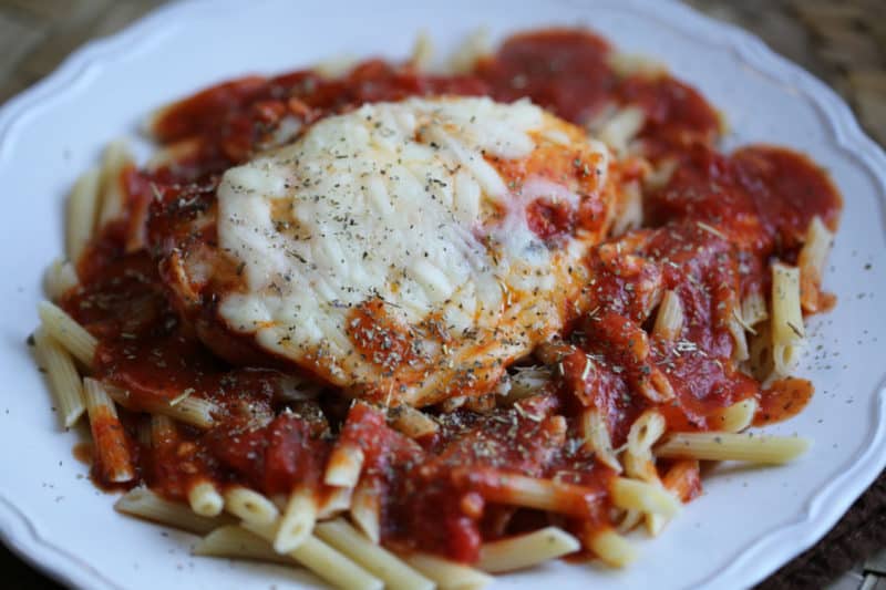 Chicken parmesan on a white plate with penne pasta and sauce