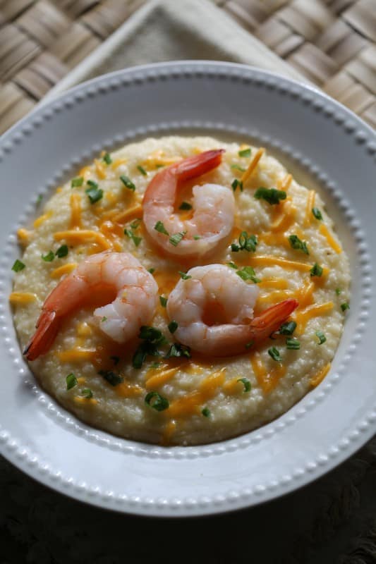 Crockpot Shrimp and Grits in a white bowl with green onion and cheddar cheese garnish