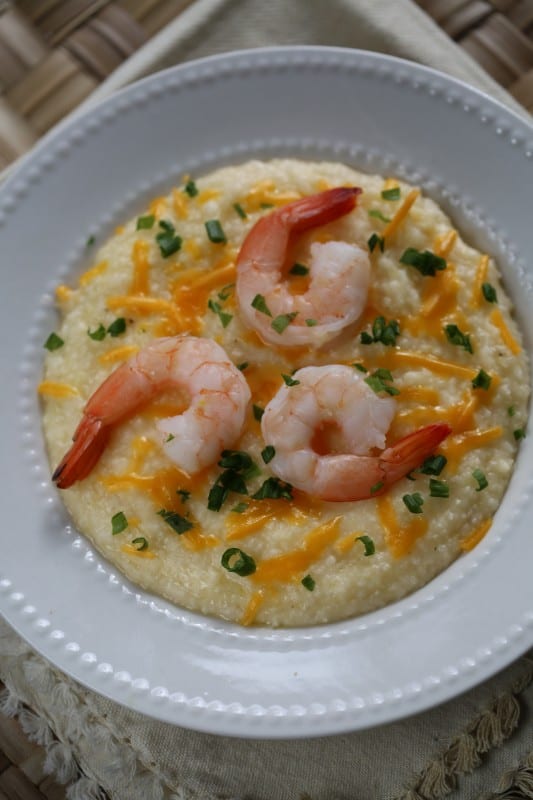 Crockpot Shrimp and Grits in a white bowl with green onion and cheddar cheese garnish