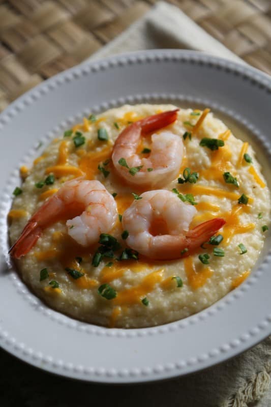 Crockpot Shrimp and Grits in a white bowl with green onion and cheddar cheese garnish