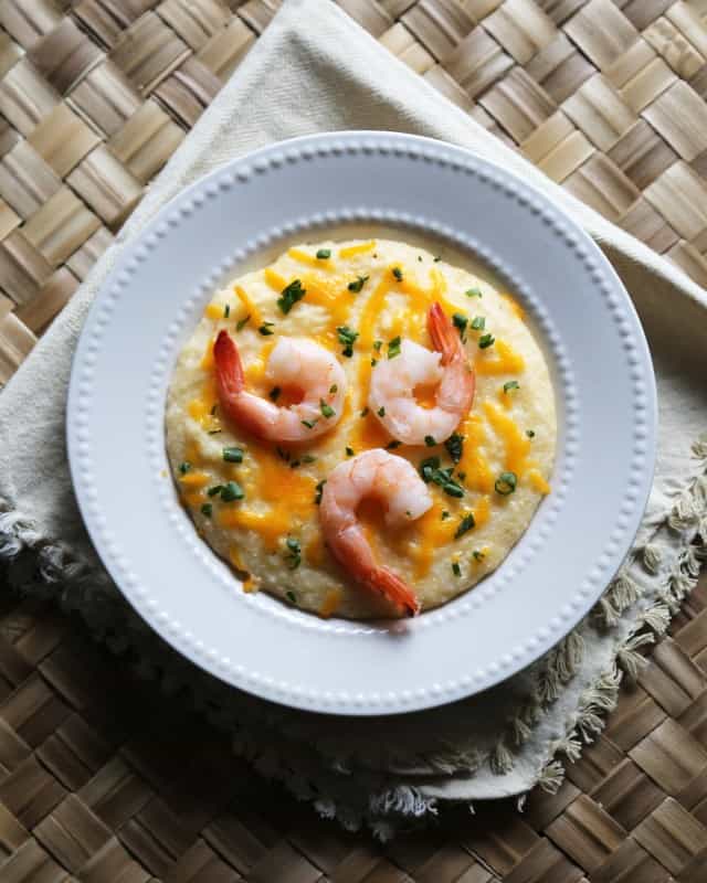 Crockpot Shrimp and Grits in a white bowl with green onion and cheddar cheese garnish