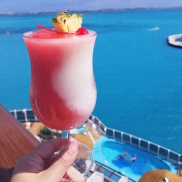 Miami Vice Cocktail in a hurricane glass with pineapple and cherry garnish with the tropical ocean in the background