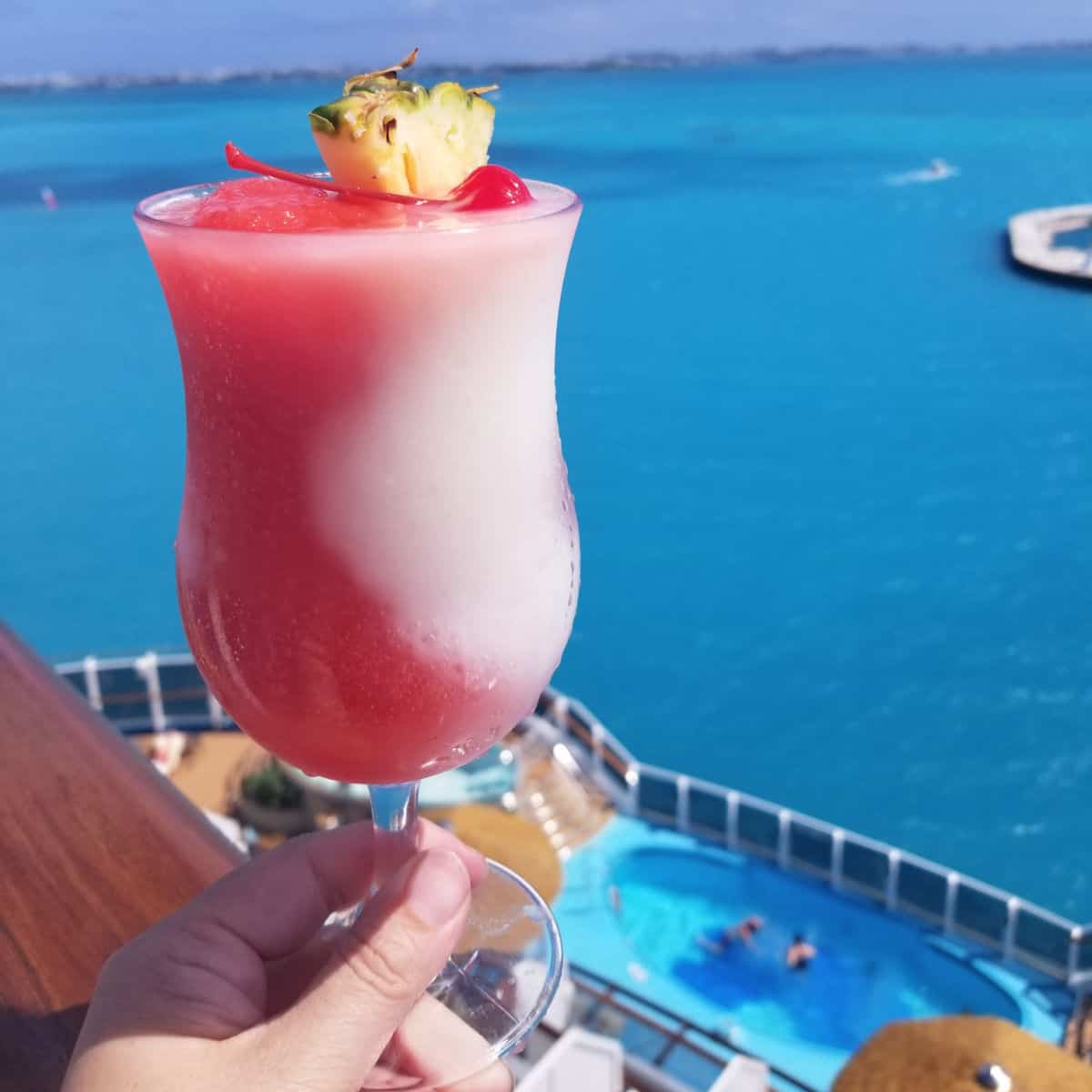Miami Vice Cocktail in a hurricane glass with pineapple and cherry garnish with the tropical ocean in the background