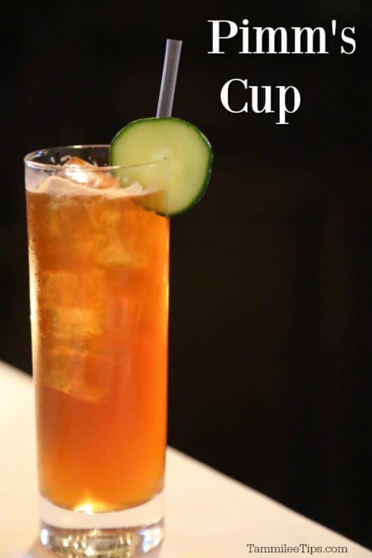 Pimms cup cocktail in a tall glass with cucumber wheel garnish and a straw