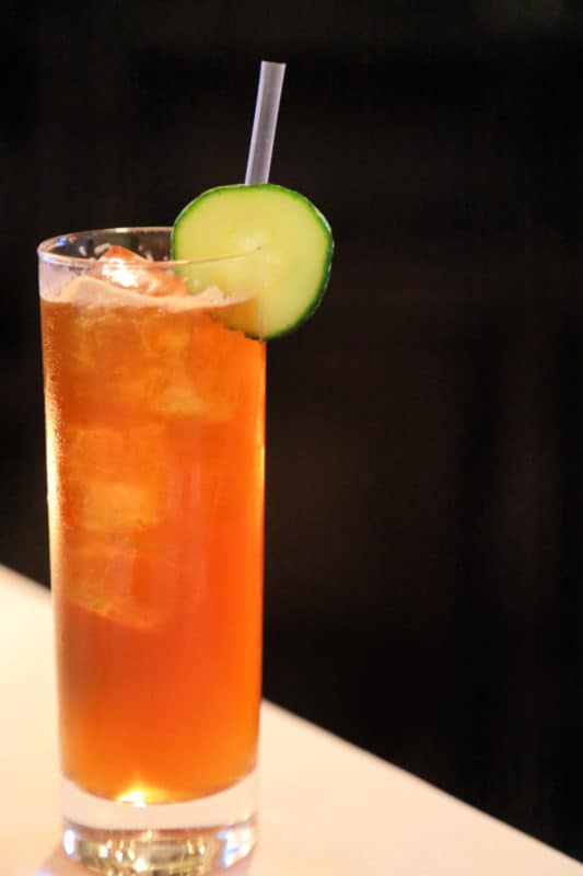 Pimms Cup cocktail in a tall glass with a cucumber wheel and straw