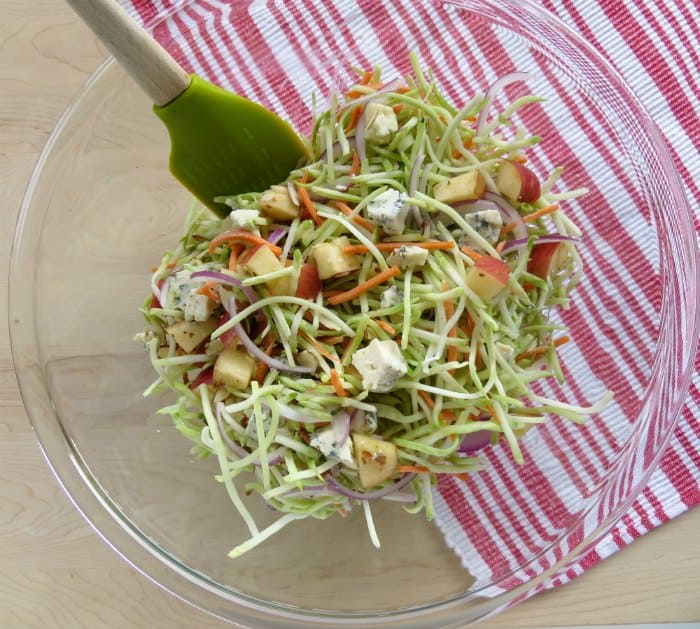 Broccoli slaw ingredients in a glass bowl with a spatula next to a red napkin