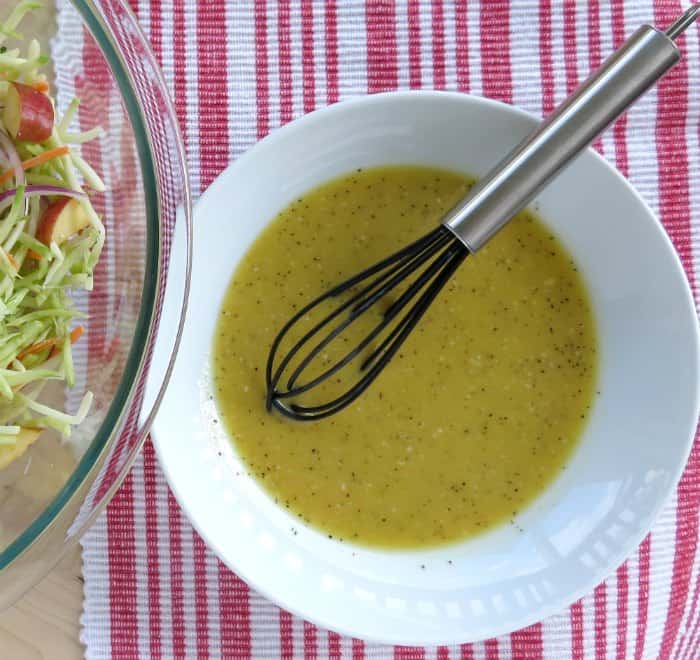 broccoli slaw dressing in a white bowl with a black whisk
