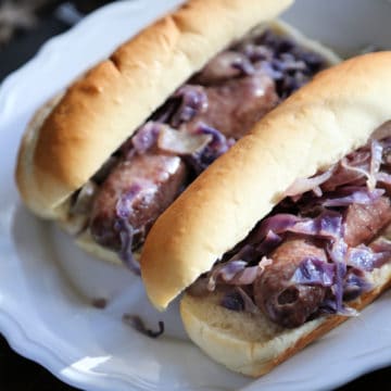 beer brats with cabbage on buns on a white plate