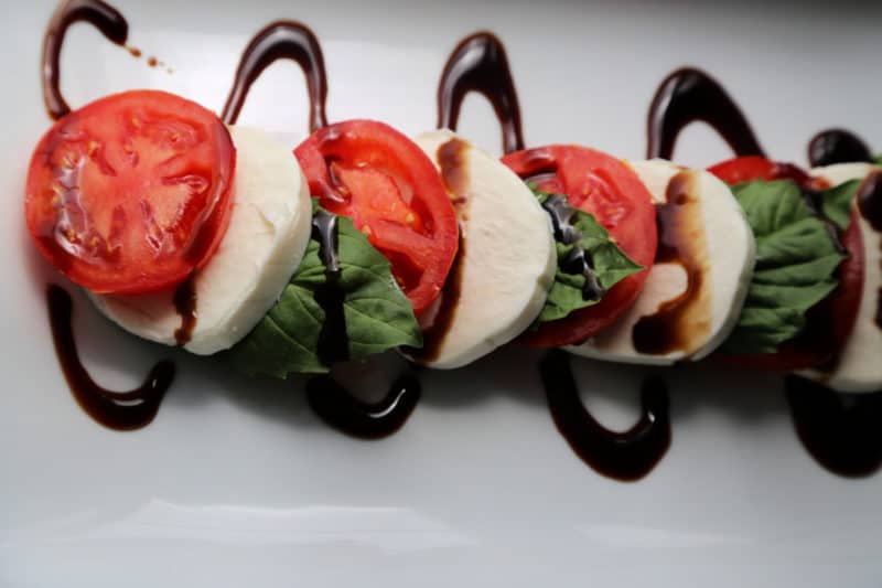 caprese salad with tomato slices, mozzarella, and basil with a drizzle of balsamic glaze on a white platter