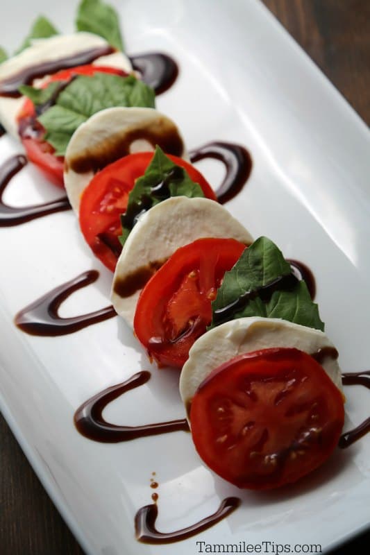 Tomato slices, mozzarella, basil leaves on a platter with balsamic glaze. 