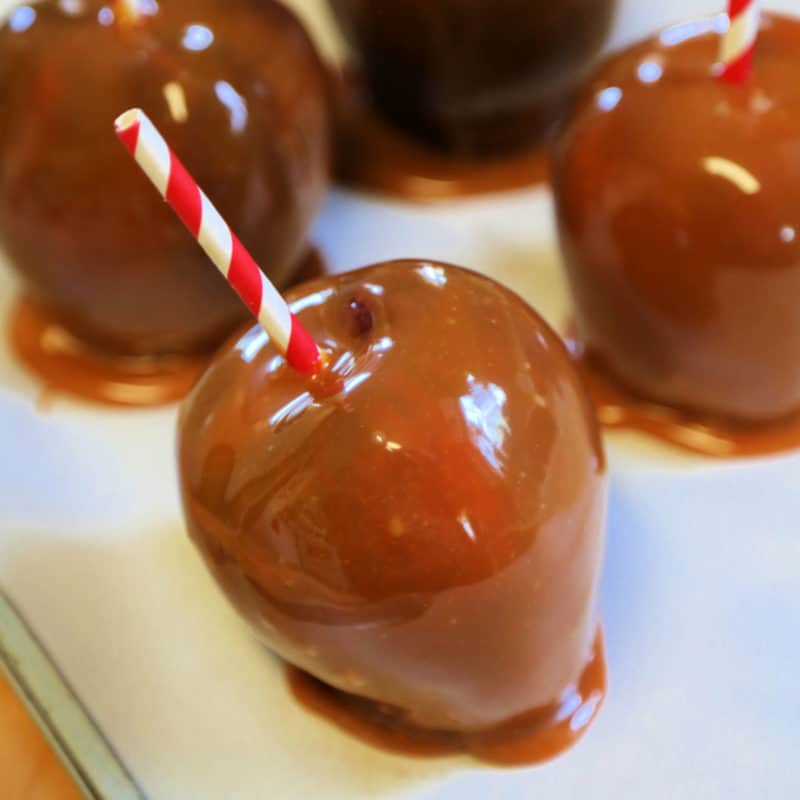 Crockpot Caramel Apples on parchment paper with red striped paper straws