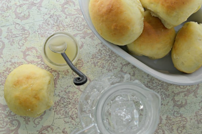 lemon butter in a glass jar next to a bowl of rolls