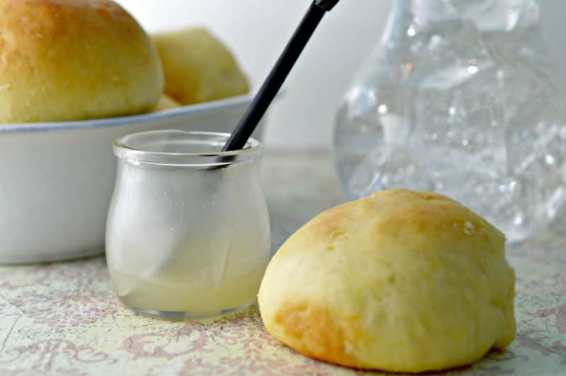butter in a glass jar with a knife next to rolls