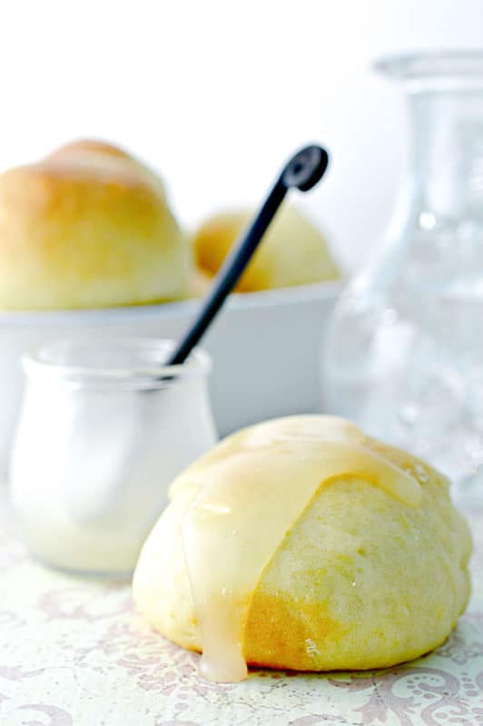 Lemon butter on top of a roll next to a jar with a spoon in it and a bowl of rolls