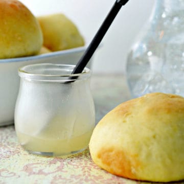 lemon butter in a glass jar next to a roll with a bowl of rolls in the background.