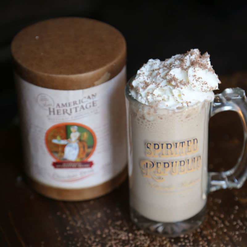 Boozy Hot Chocolate garnished with whipped cream in a glass mug next to American Heritage chocolate