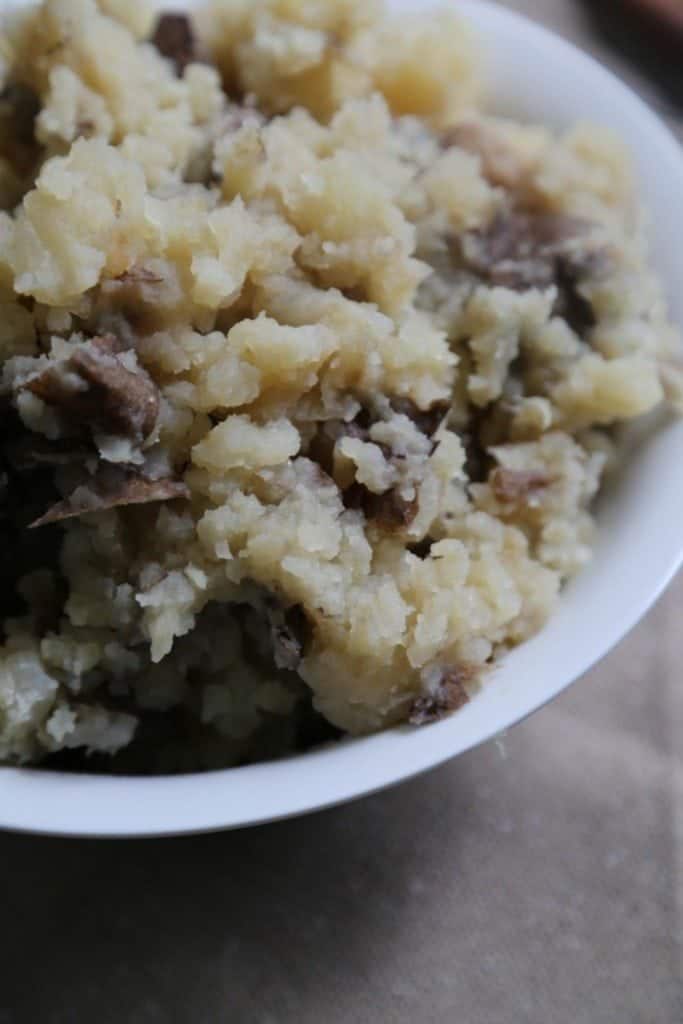 Crock Pot Garlic Mashed Potatoes in a white serving bowl on a brown placemat