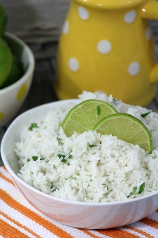 Cilantro Lime Rice in a white bowl with lime wedges next to a yellow pitcher