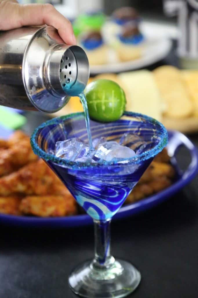 Blue cocktail pouring into a martini glass with a football lime