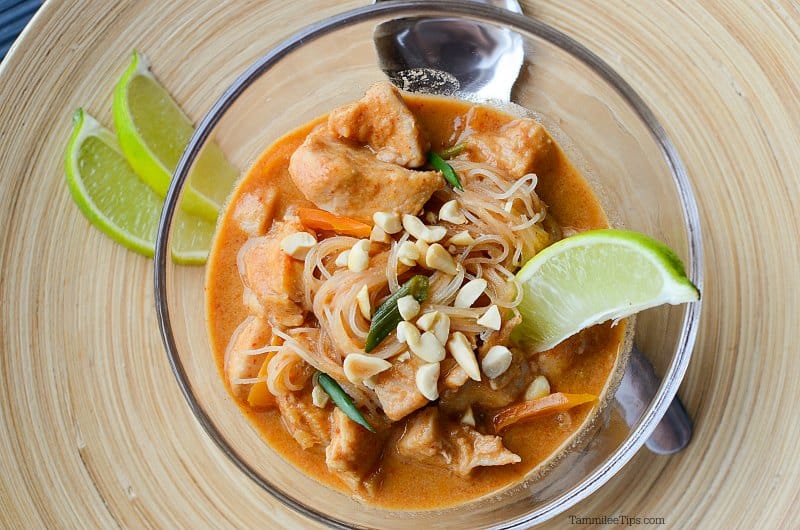 Thai chicken stew in a glass bowl with a lime slice on a wooden plate with more limes and a spoon