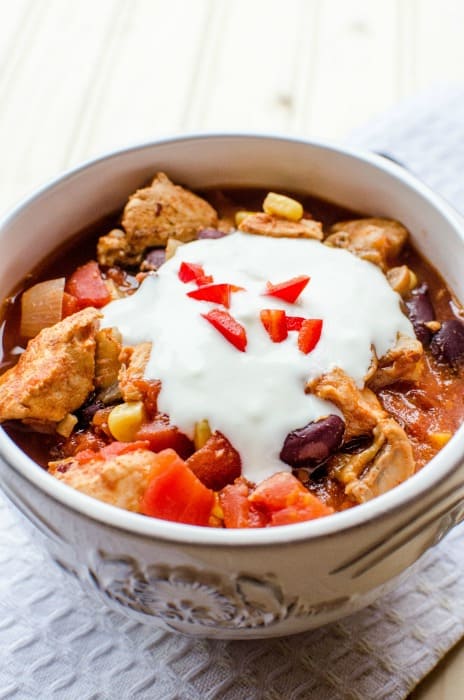 bowl of chili topped with sour cream, next to a silver spoon on a white napkin