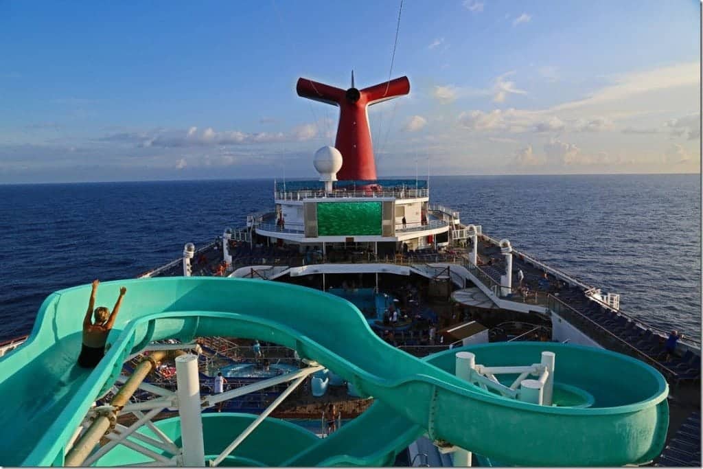 Women on a water slide on a cruise ship with the Carnival Cruise funnel and movie playing on the big screen with the ocean surrounding the cruise ship 