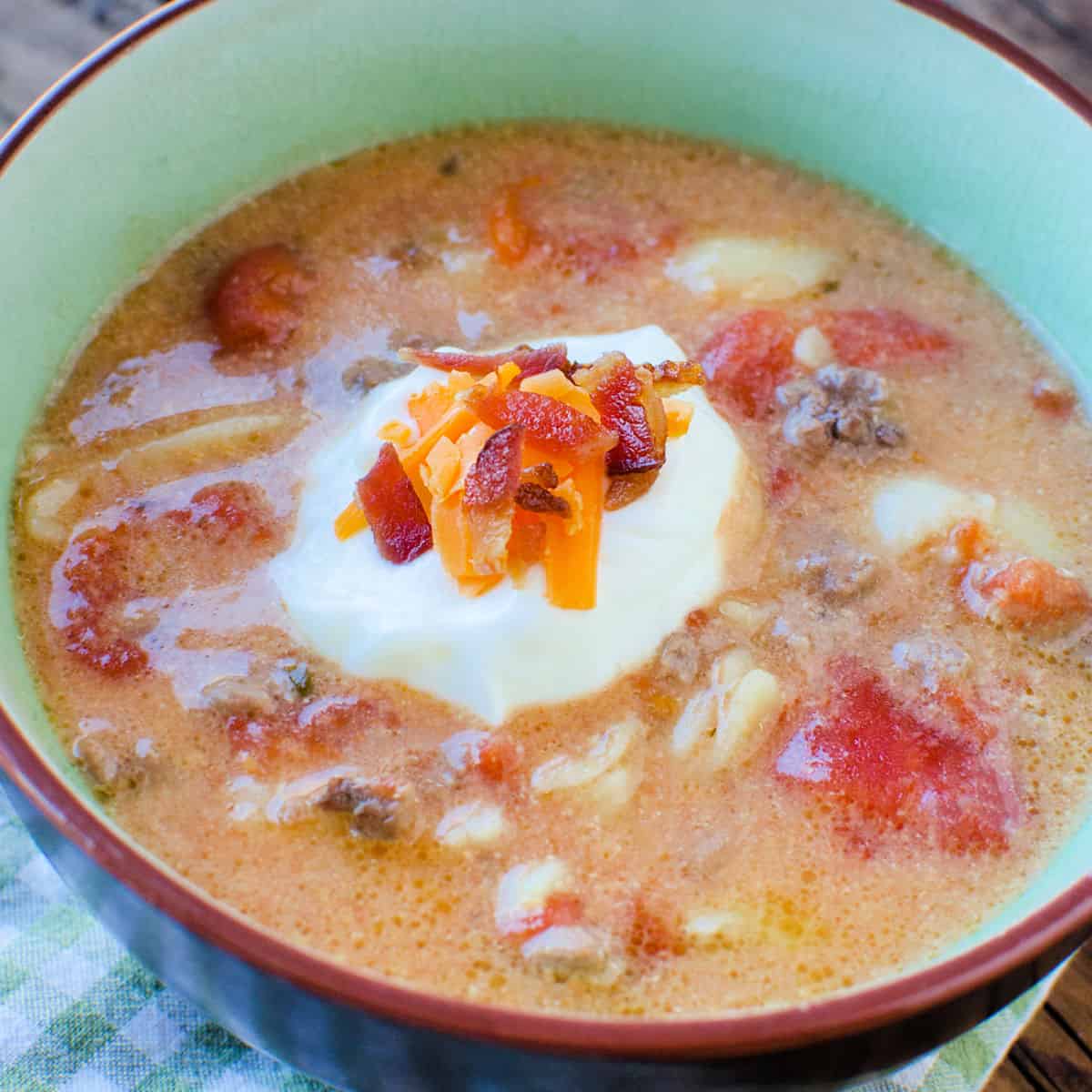 Cheeseburger soup garnished with sour cream, cheese, and bacon in a bowl