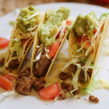 taco meat in a taco shell with shredded lettuce, tomatoes and guacamole