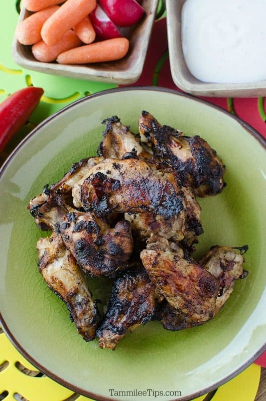 Jamaican Jerk Chicken wings on a green plate next to a bowl of carrots and radishes, 