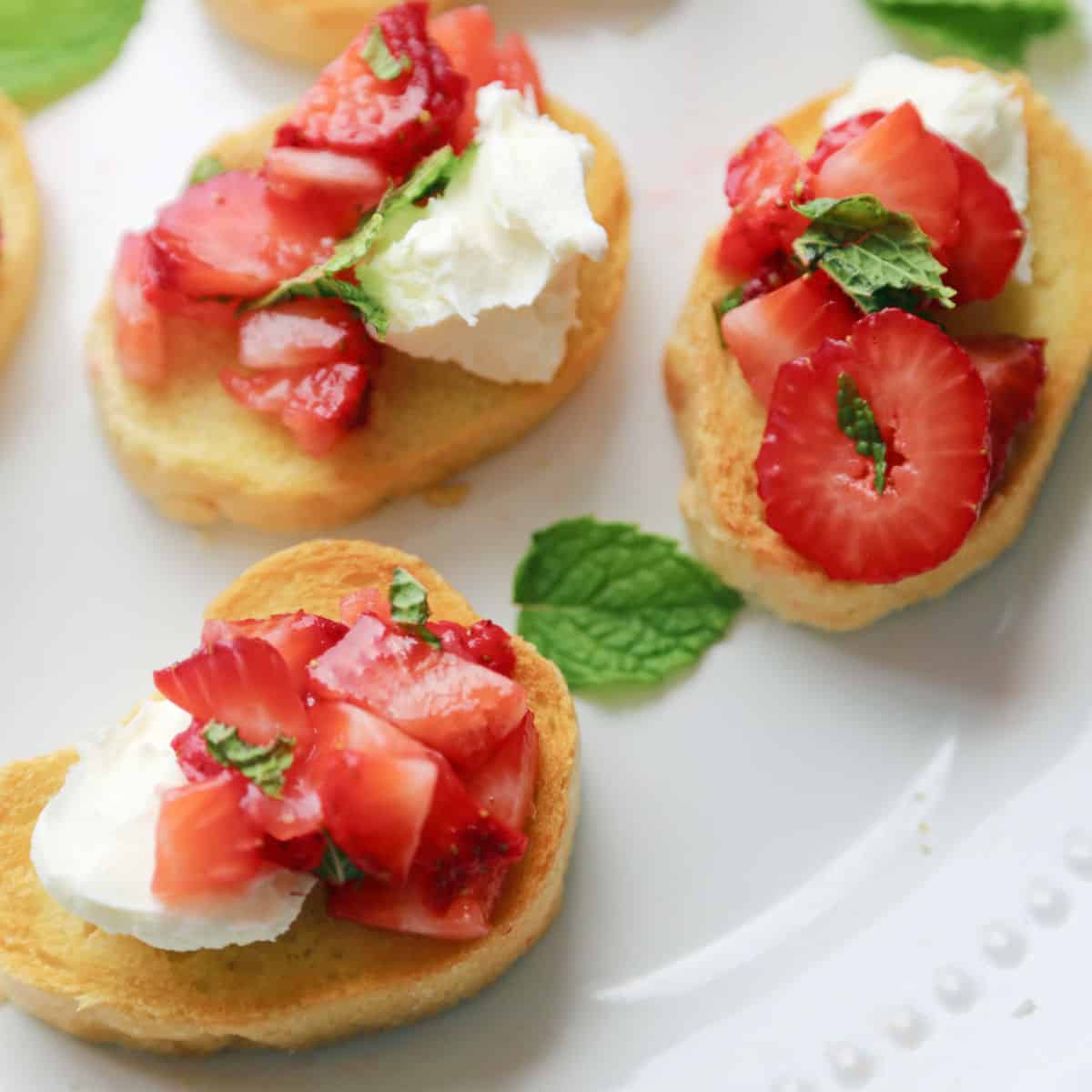Slices of strawberry bruschetta on a white serving dish with mint leaves