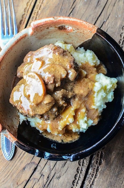 Salisbury steak over potatoes in a pottery bowl next to a fork