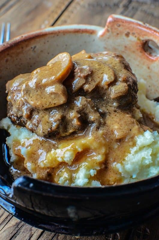 Salisbury steak over potatoes in a pottery bowl next to a fork