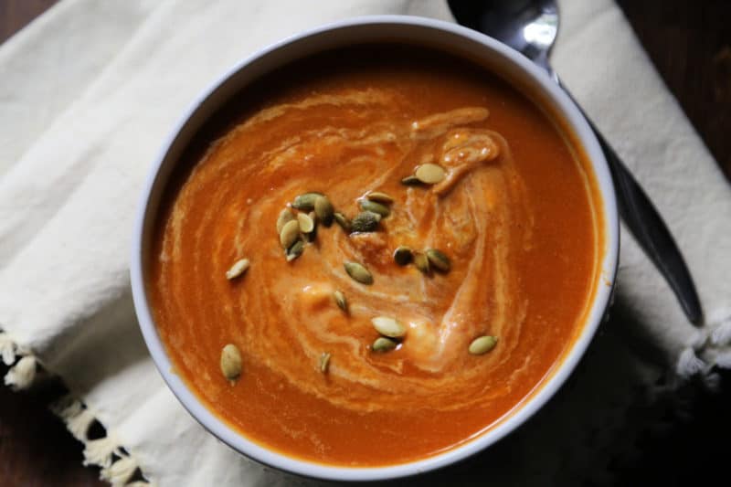 pumpkin soup topped with seeds in a white bowl next to a spoon