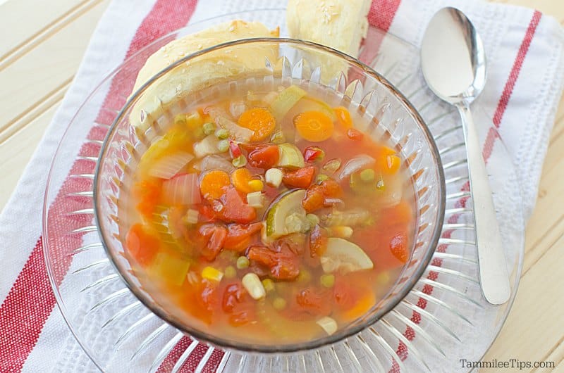 vegetable soup in a glass bowl on a plate next to a spoon