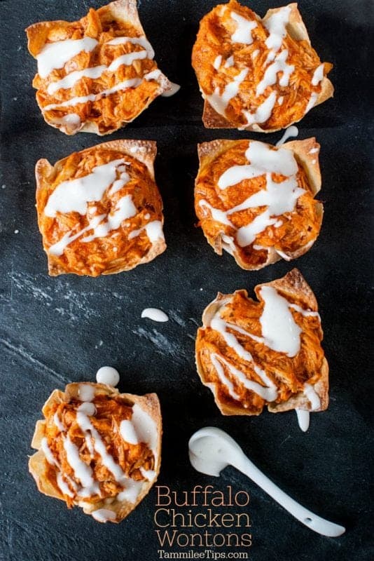 Buffalo chicken wontons on a dark board with a spoon of dressing