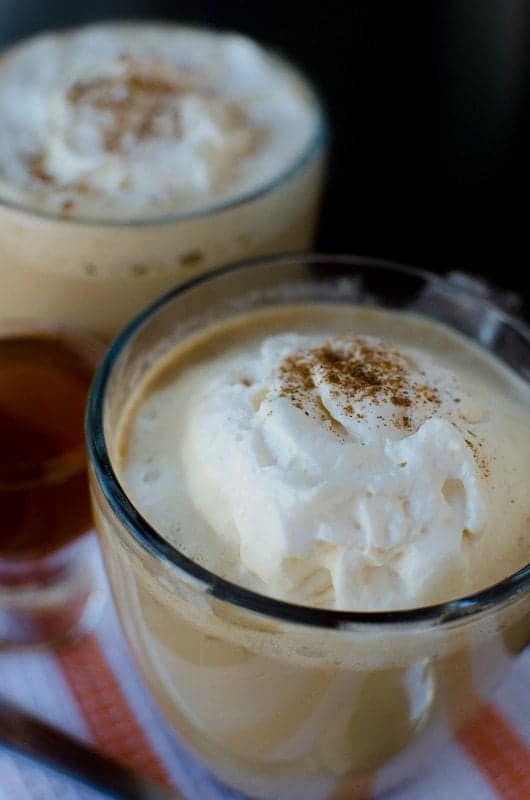 crockpot pumpkin spice lattes with whipped cream on top and cinnamon in a clear glass mug