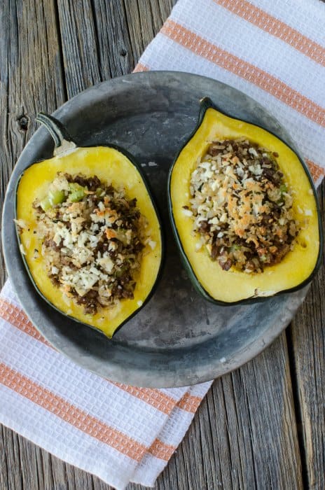 2 stuffed acorn squash with sausage and rice on a plate on top of a white cloth napkin