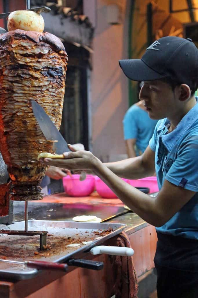 male with a large knife cutting meat off of a large skewer spinning