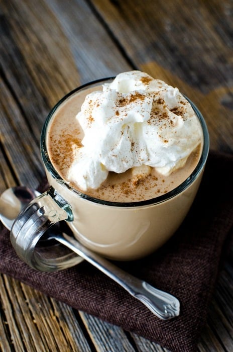 glass mug with Mexican hot chocolate topped with whipped cream and cinnamon next to a silver spoon