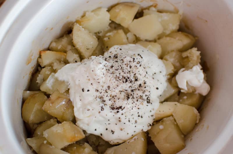 sour cream and seasoning on cooked potatoes in a slow cooker bowl