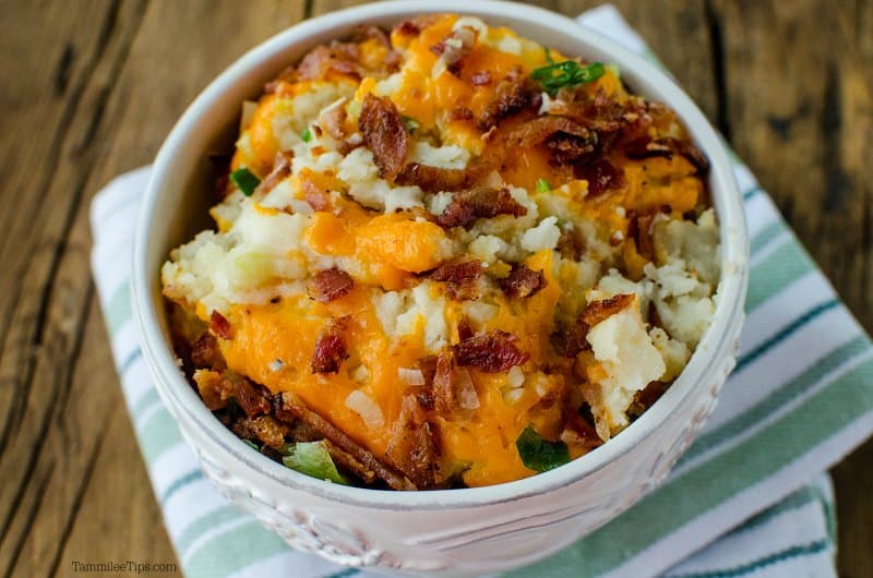 White bowl filled with mashed potatoes, cheese, green onions, and bacon. 
