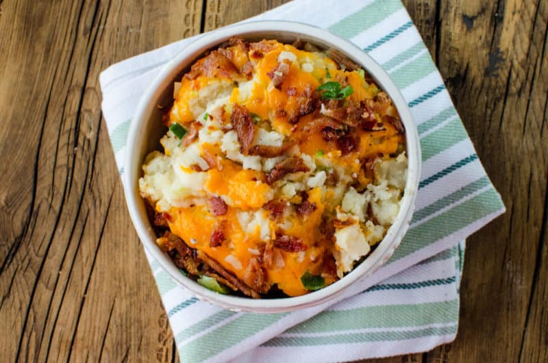 bacon and cheese on loaded mashed potatoes in a white bowl on a cloth napkin