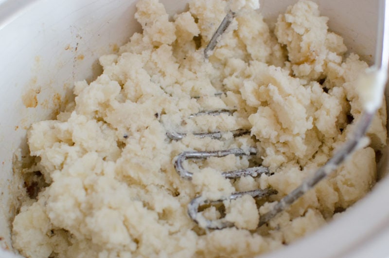 Potato masher mashing potatoes in a slow cooker