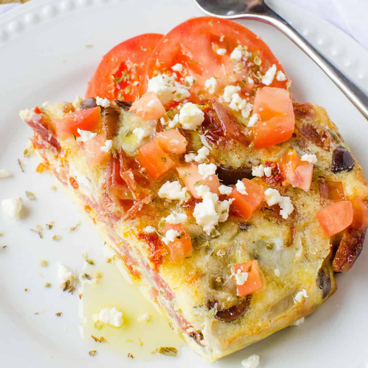 Greek Frittata on a white plate garnished with tomatoes and feta